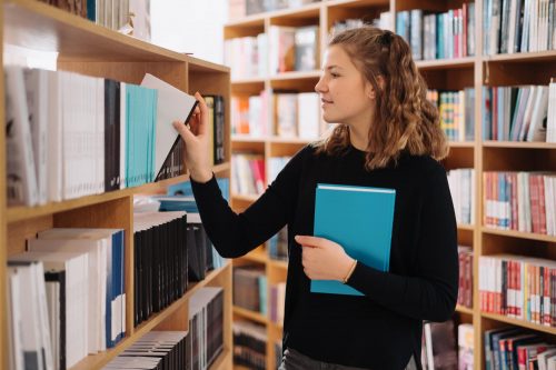 teenager-girl-picking-book-on-library-shelf Chica en la biblioteca